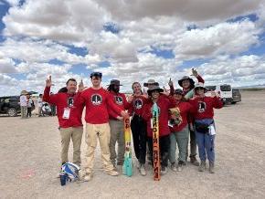 The Aerobears team pose with their 2024 rocket and show the LR hand sign in the New Mexico desert